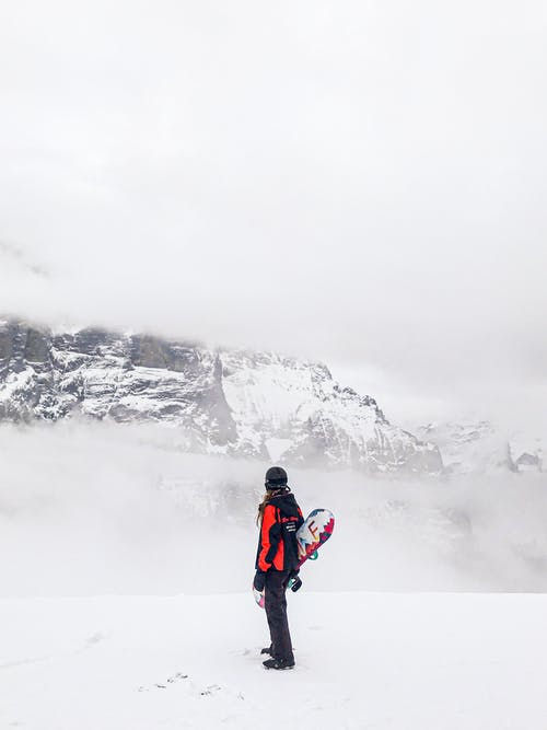 红色外套和黑裤子的人站立在积雪的地面上 · 免费素材图片