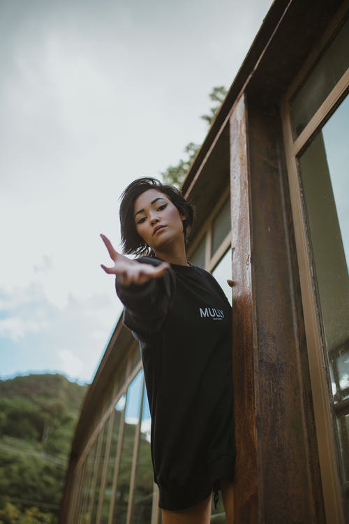 站在棕色木门旁边的黑色长袖衬衫的女人 · 免费素材图片