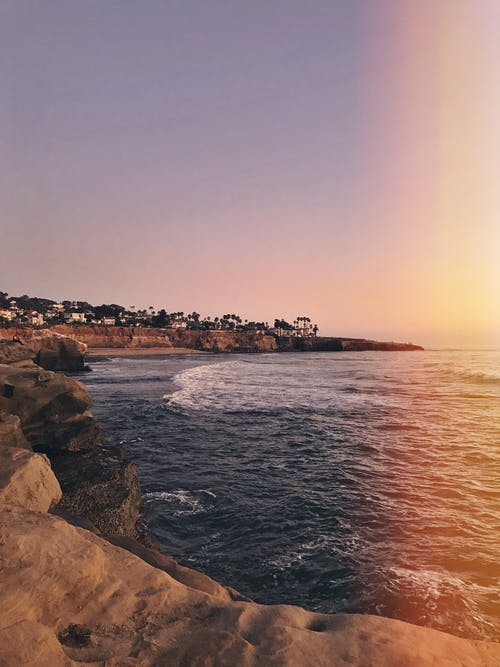 在日落期间在岩石海岸附近挥舞着的海 · 免费素材图片