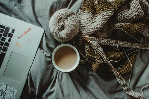 咖啡杯和针织物放在上网本附近的床上 · 免费素材图片
