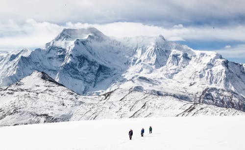 无法识别的人在白雪皑皑的地形在山附近行走 · 免费素材图片