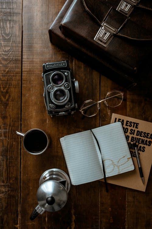 棕色木制的桌子上的白色陶瓷杯旁边的黑色相机 · 免费素材图片