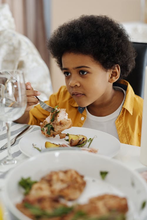 男孩坐在一张桌子的食物在他的盘子上 · 免费素材图片