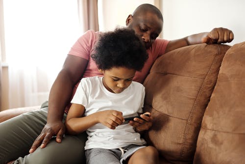 父亲看着他的儿子在智能手机上玩 · 免费素材图片