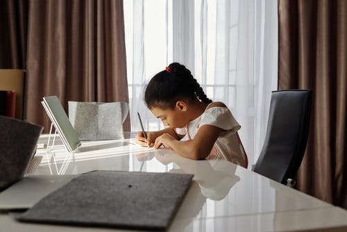 小女孩坐在一张桌子和写作 · 免费素材图片