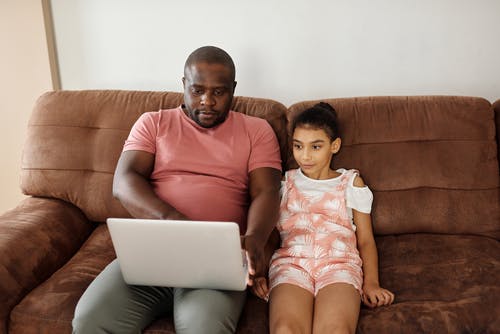 父亲和女儿坐在沙发上，看着一台笔记本电脑 · 免费素材图片