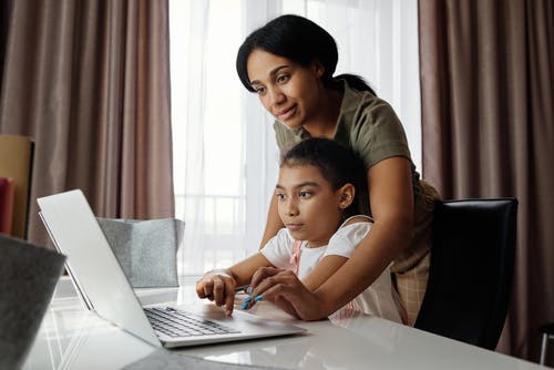 母亲帮助她的女儿使用一台笔记本电脑 · 免费素材图片