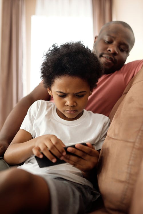 父亲看着他的儿子在智能手机上玩 · 免费素材图片