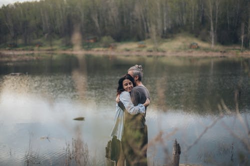 幸福的情侣拥抱在平静的湖面附近 · 免费素材图片