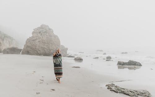 女人裹在毯子里走在沙滩上 · 免费素材图片