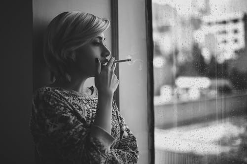在雨期间窗口附近的忧郁女人吸烟 · 免费素材图片