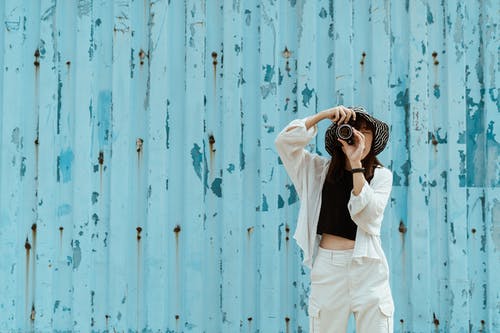 无法识别的摄影师在蓝色墙附近的相机拍照 · 免费素材图片