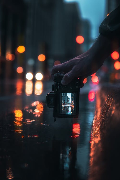 拿着黑单反相机的人在夜间拍摄城市的灯光 · 免费素材图片