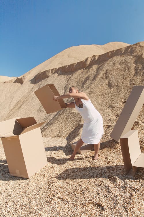 非正式的年轻女子，在晴朗的一天在沙漠中携带纸箱 · 免费素材图片