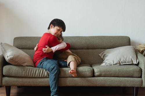 两个孩子坐在灰色的沙发上互相拥抱的照片 · 免费素材图片