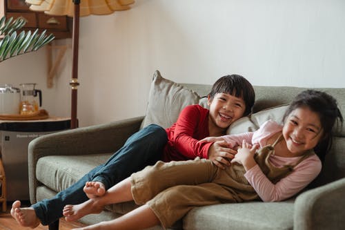 两个孩子坐在灰色的沙发上玩的照片 · 免费素材图片