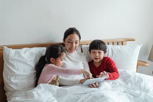 使用平板电脑时坐在床上的女人和孩子的照片 · 免费素材图片