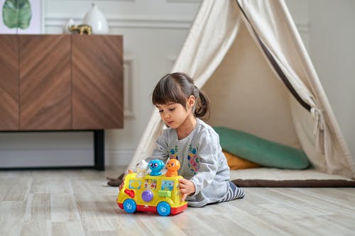 玩塑料玩具车的灰色毛衣的女孩 · 免费素材图片