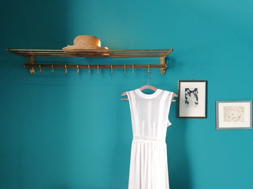 与草帽和蓝墙附近的白色连衣裙的衣架 · 免费素材图片