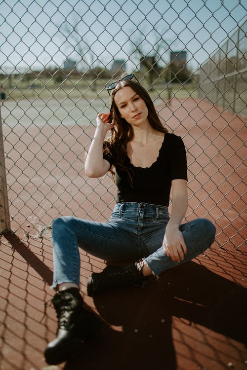 黑色背心和蓝色牛仔牛仔裤，坐在棕色混凝土地板上的女人 · 免费素材图片