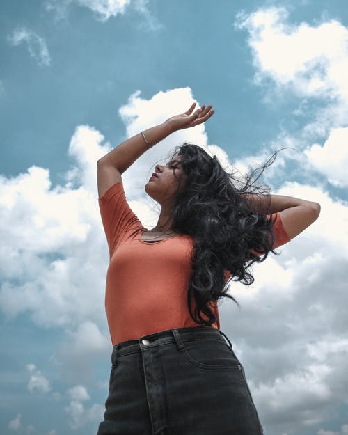 橙色背心和黑色牛仔裤，举起她的手的女人 · 免费素材图片