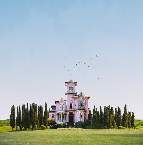 白色和粉红色的混凝土建筑，在白色的天空下的绿草田 · 免费素材图片