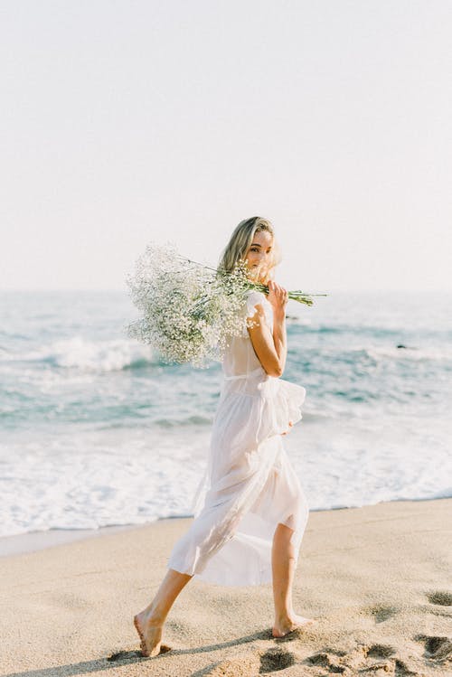 白色礼服站在海滩岸边的女人 · 免费素材图片