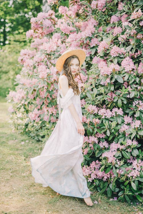 站在粉红色的花朵旁边的白色连衣裙的女人 · 免费素材图片
