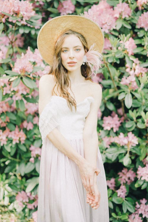 白色无袖连衣裙戴着棕色太阳帽子站在粉红色的花朵附近的女人 · 免费素材图片