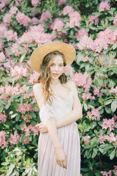穿棕色太阳帽子站在粉红色的花朵附近的白色连衣裙的女人 · 免费素材图片