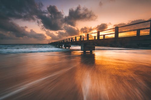 在日落时海沙滩上的行人天桥 · 免费素材图片