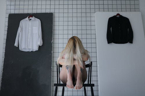 匿名沮丧的妇女坐在铺磁砖的墙壁后的椅子 · 免费素材图片