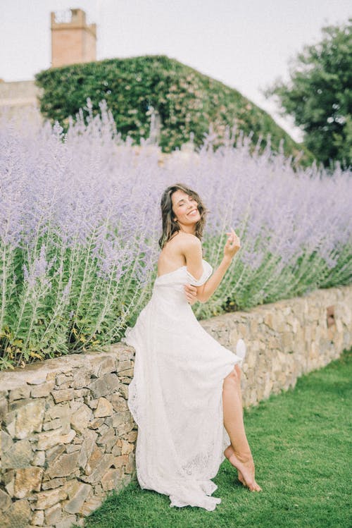 坐在紫色的花旁的白色婚纱的女人 · 免费素材图片