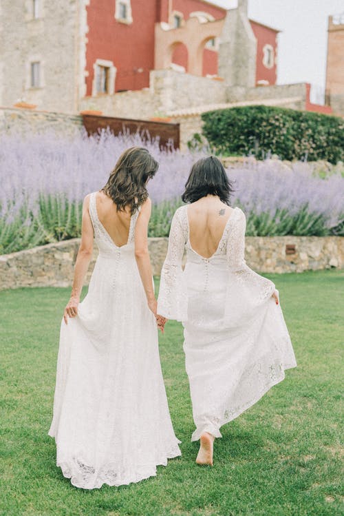 穿着白色婚纱的两个女人在草地上行走的照片 · 免费素材图片