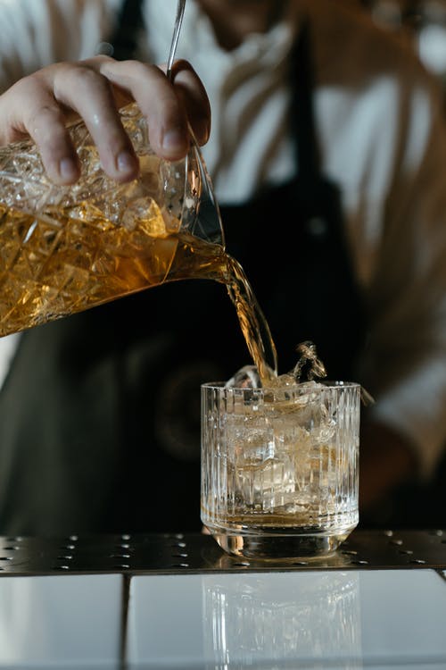 将棕色液体倒在透明的水杯上的人 · 免费素材图片