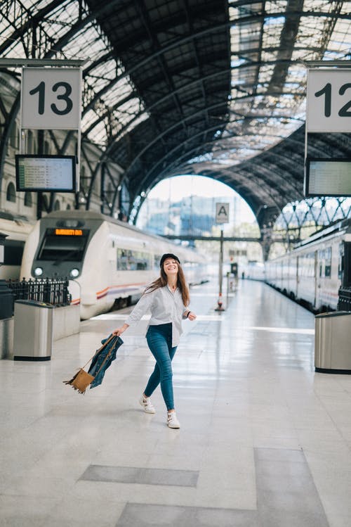 站在火车站的平台上的白色长袖衬衫和蓝色牛仔牛仔裤的女人 · 免费素材图片