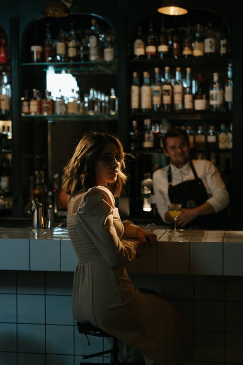 站在酒吧柜台前的灰色长袖连衣裙的女人 · 免费素材图片