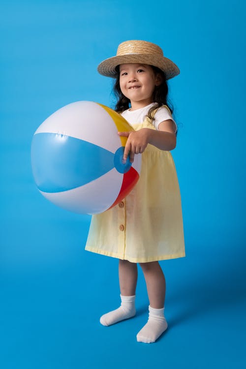 拿着白色蓝色和黄色充气球的棕色礼服的女孩 · 免费素材图片