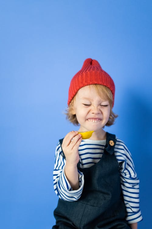 红色针织帽和黑色和白色条纹衬衫的男孩吃黄色水果 · 免费素材图片