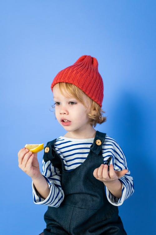 拿着黄色塑料玩具的黑白条纹衬衫和红色针织帽的男孩 · 免费素材图片