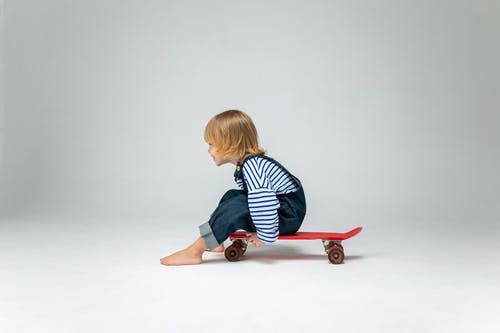 坐在红色滑板上的黑色和白色条纹长袖衬衫的男孩 · 免费素材图片