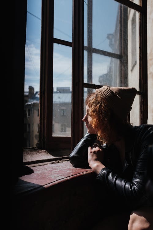 坐在窗口旁边的黑色皮夹克和棕色针织帽的女人 · 免费素材图片
