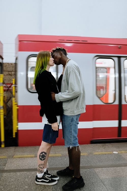 站在红色和白色火车旁边的白色连帽衫的女人 · 免费素材图片