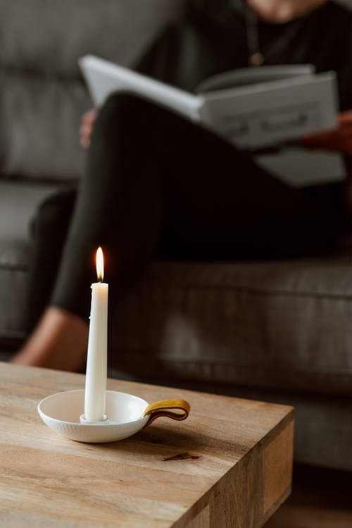 在沙发上无法辨认的女人阅读本书附近燃烧的蜡烛 · 免费素材图片
