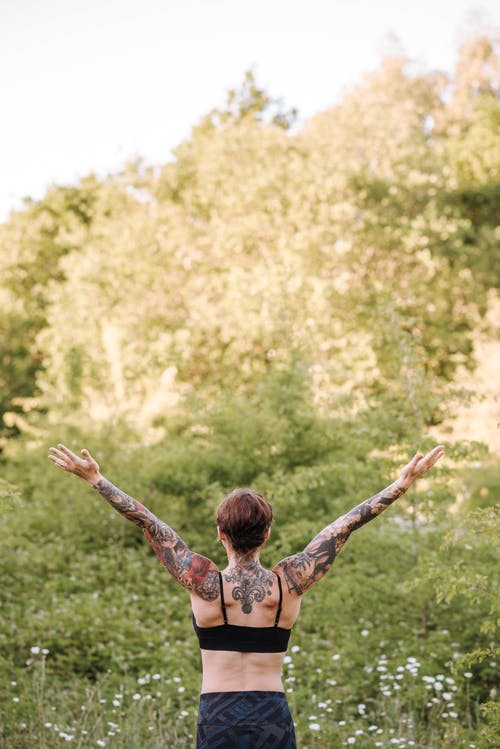 认不出来的纹身的女人练习瑜伽对绿树 · 免费素材图片