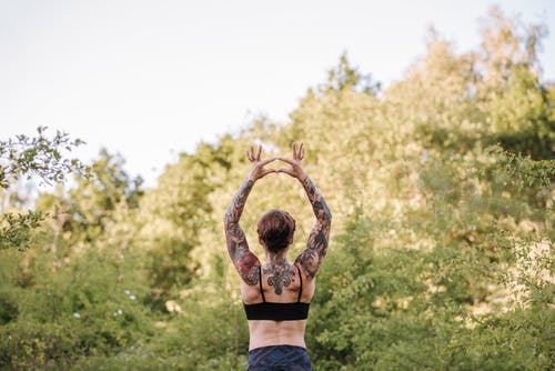 认不出来的纹身的女人练习瑜伽对郁郁葱葱的树木 · 免费素材图片