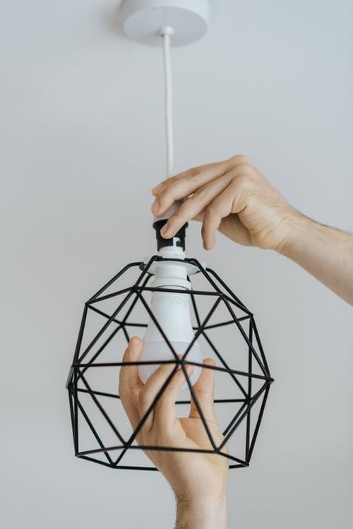 匿名男子在家中将灯泡拧入金属灯 · 免费素材图片