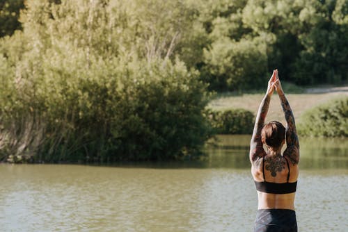 匿名纹身的女人在夏天练习瑜伽对河 · 免费素材图片
