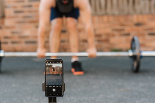 无法识别的健美运动员在城里的智能手机录制视频后举杠铃 · 免费素材图片