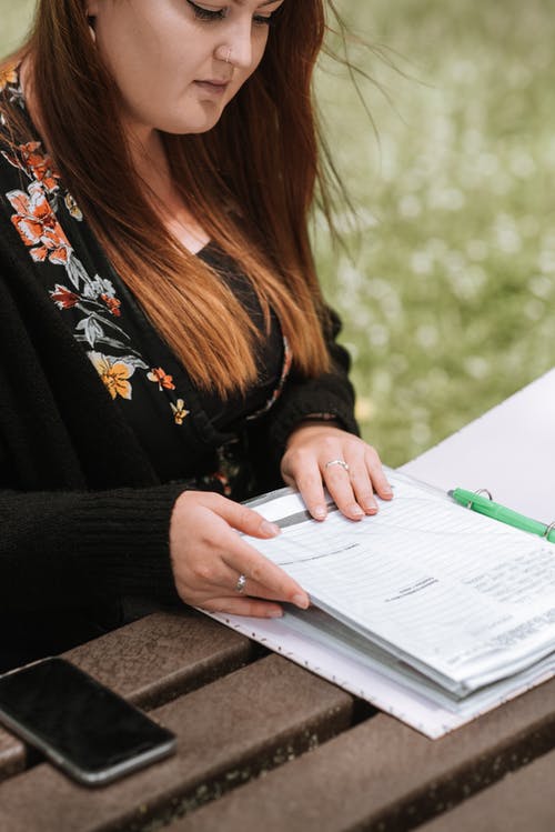 作物女人坐在公园的桌旁，阅读文档 · 免费素材图片